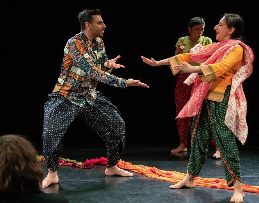 Photo of the performers facing each other and making dance gestures towards each other. Colourful scarves are laid in a line on the floor of the performance space.