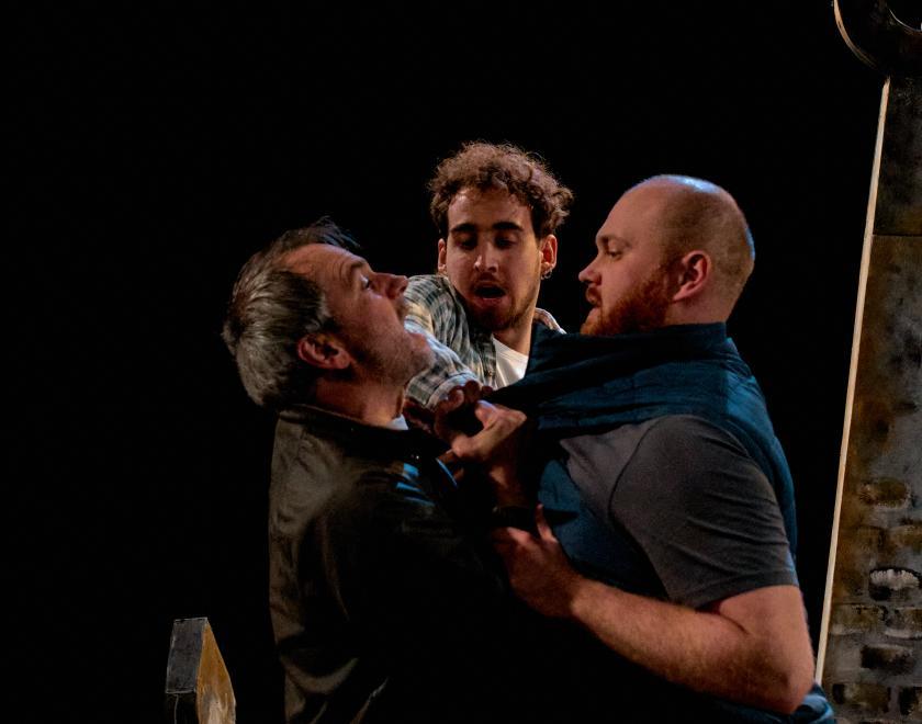 Two performers appear to be in the midst of a fight or altercation, as a third performer attempts to break them apart. 