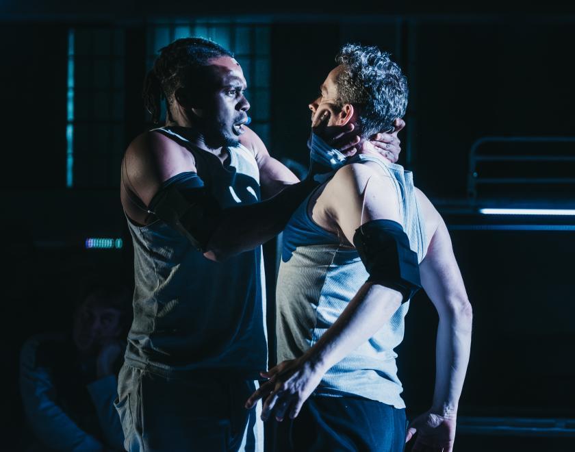 Photo of two performers close together, in what could be a fight or a romantic clinch. One has his hands around the other's face.