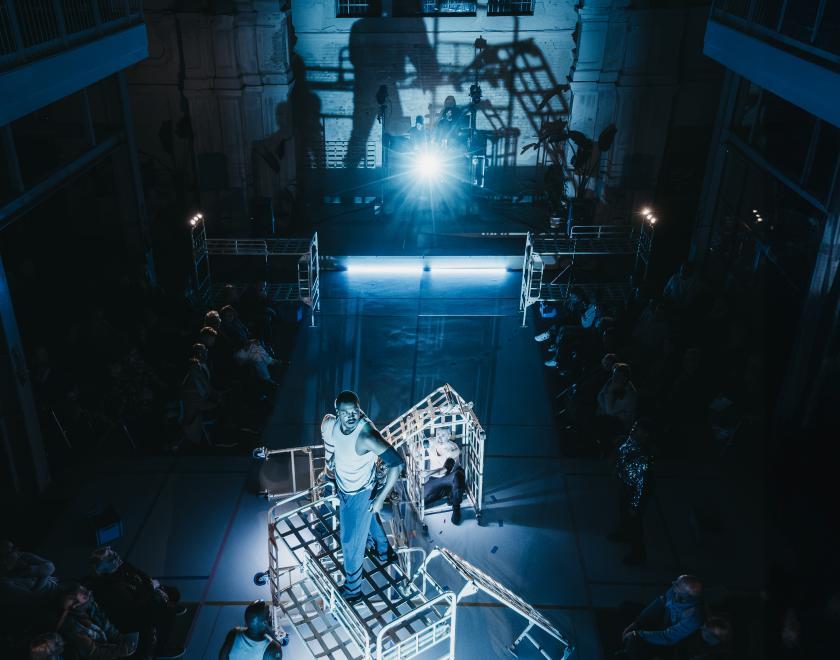 Photo of the full stage, which has a structure made out of prison beds and performers standing or crouching around it