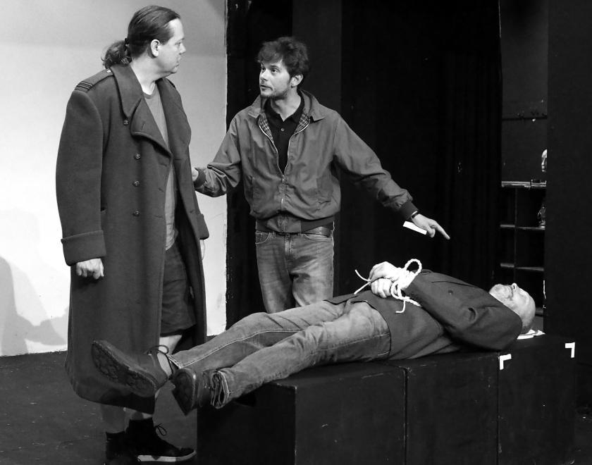 2 men are talking, 1 man is unconscious and tied up