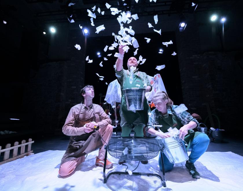 Photo of three performers gathered around a upward-facing fan, holding silver buckets and throwing pieces of paper into the airstream.  Fourth image: Photo of a performer dressed as a snowman with a hat, scarf and carrot nose, holding two sticks for arms.