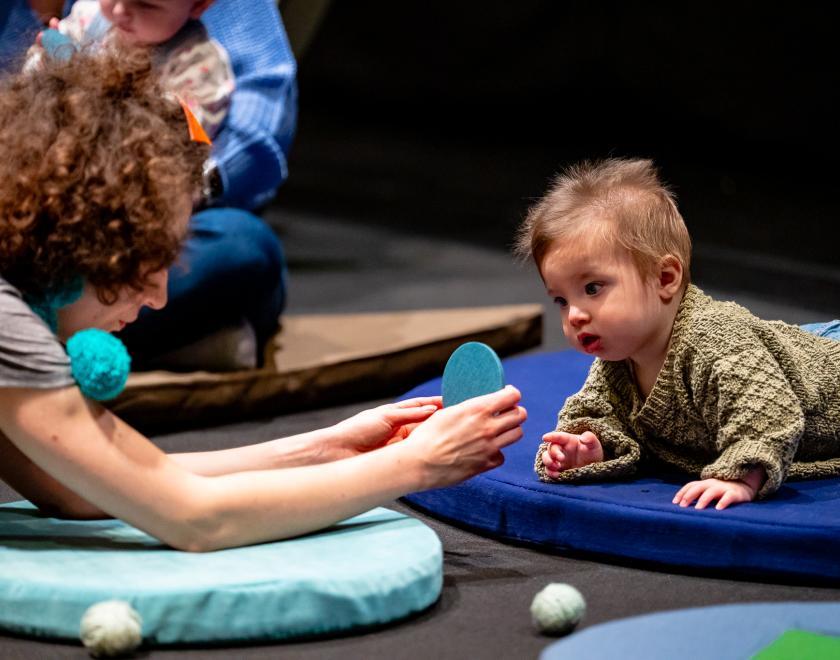 Photo of the performer holding a flat blue disc out to a fascinated baby.