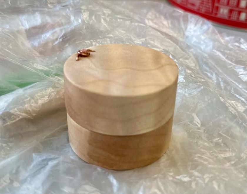 A round wooden ring box with pin hinge open.