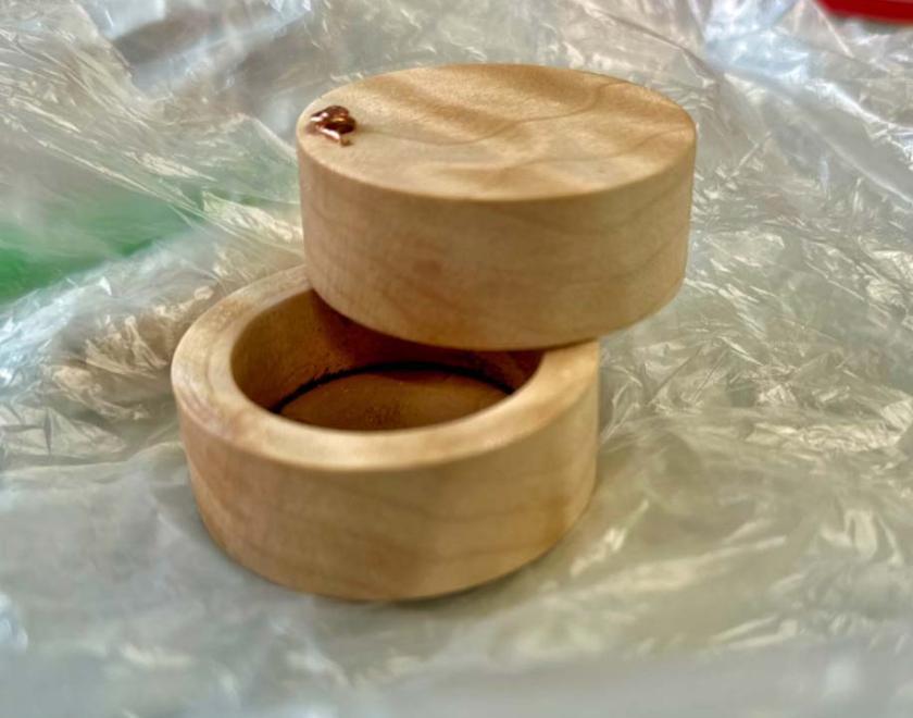 A round wooden ring box with pin hinge closed.