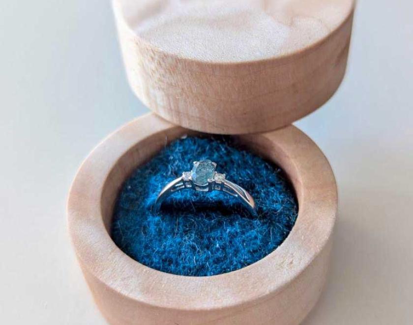 Maple ring box with blue felt insert holding an engagement ring.