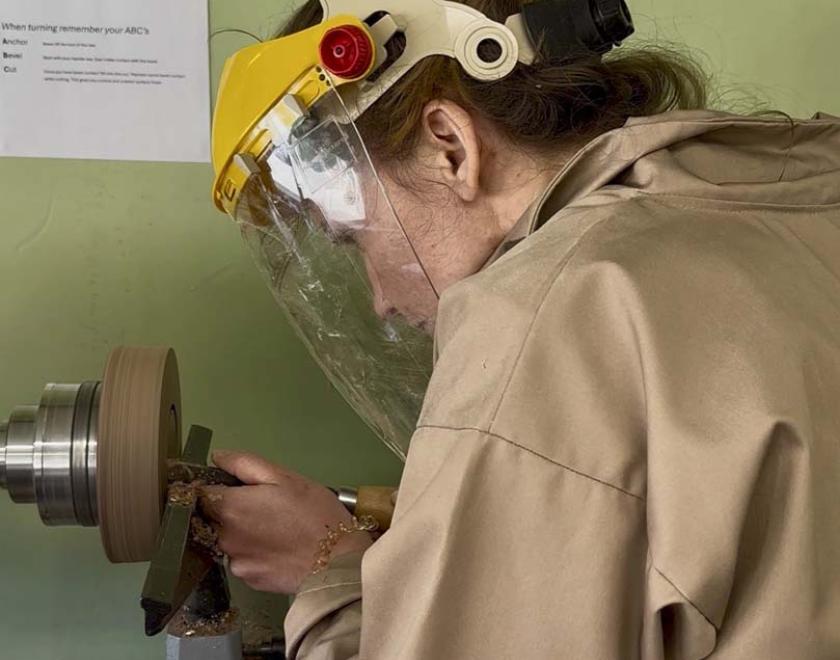 A woman turning a wooden bowl on the lathe.