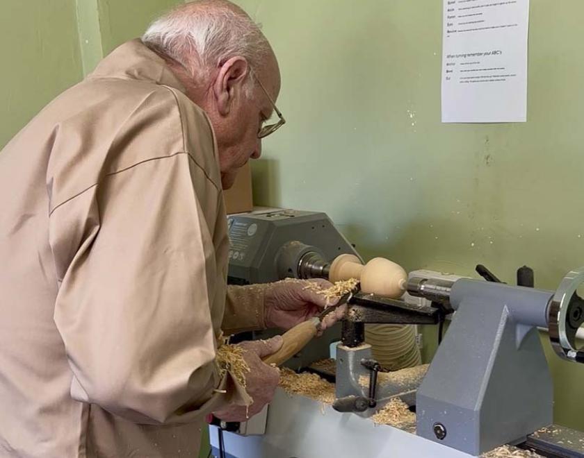 A man turning a wooden mushroom on a lathe.
