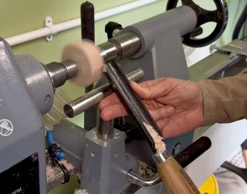 A woman shaping her special piece of wood on the lathe using a roughing gouge.