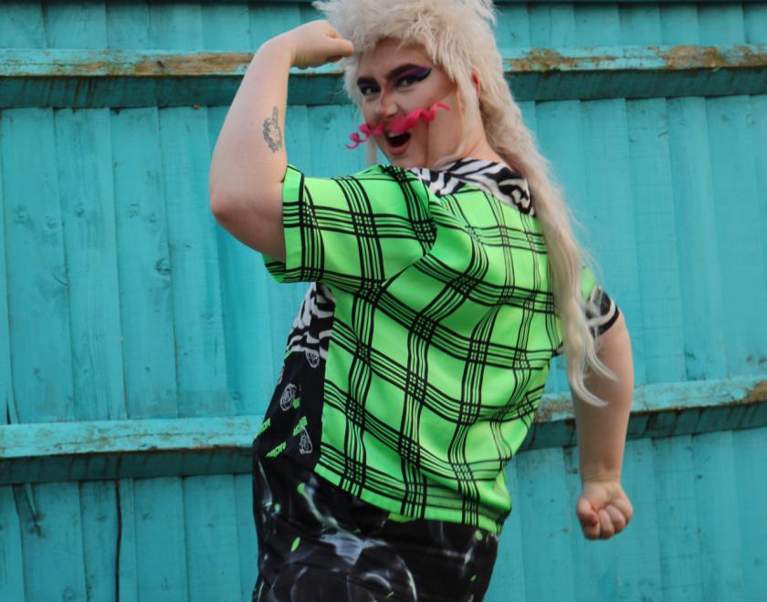A drag artist posing in a strongman position, with a smile