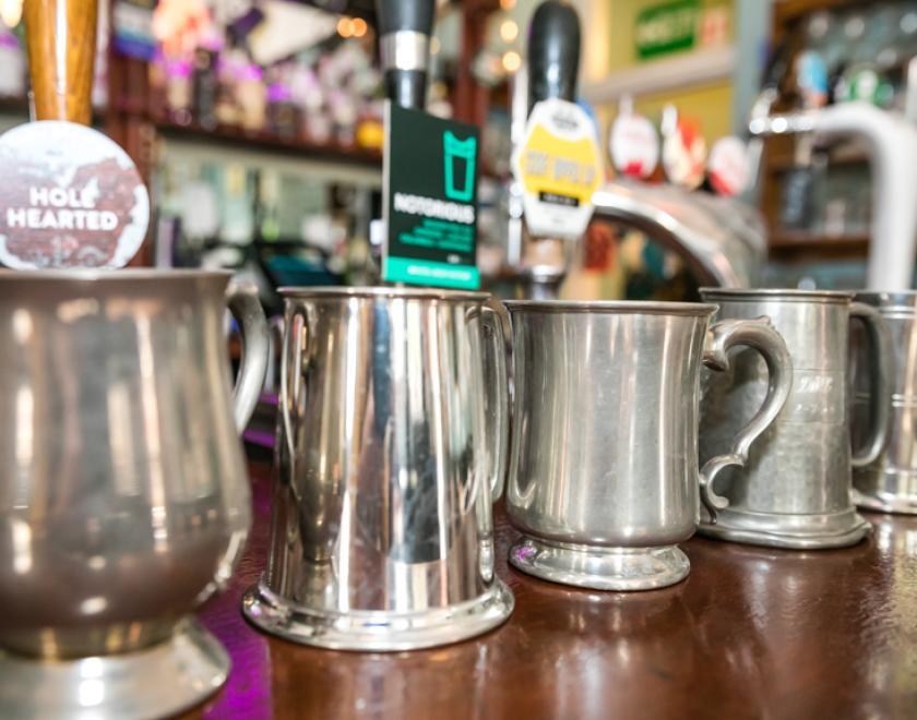 Pewter tankards on a bar top with handpulls behind