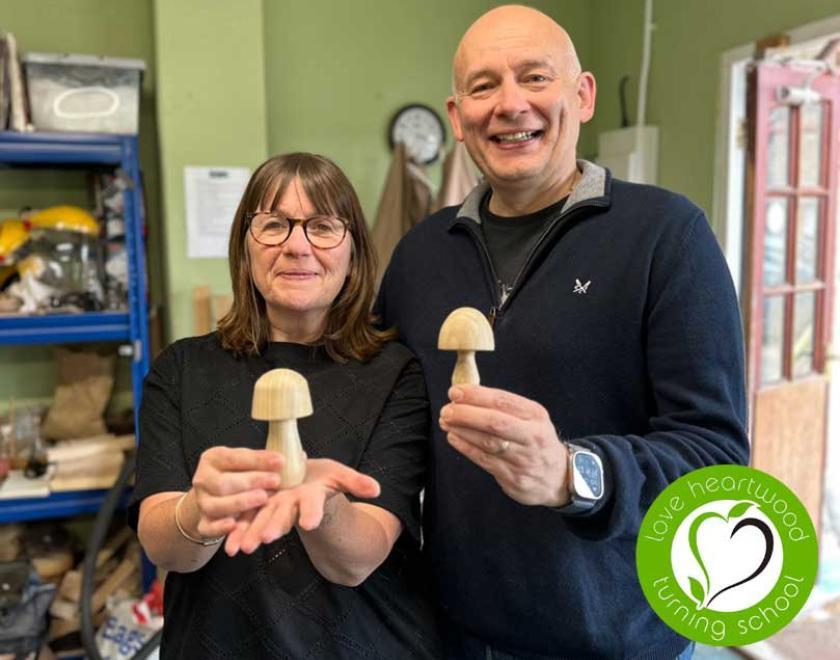 Husband and wife each holding a wooden mushroom.