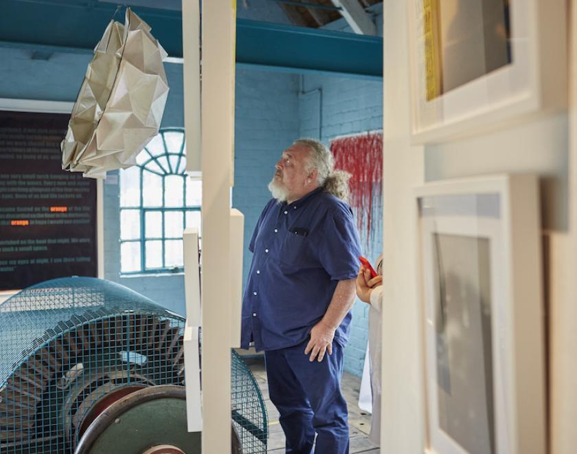 man in blue shirt looking up at white abstract sculpture hanging 