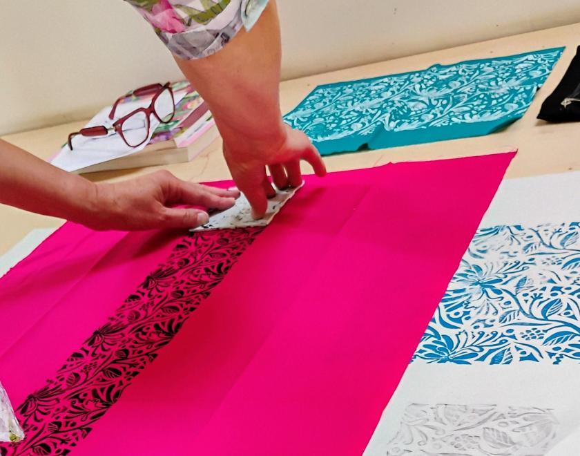 Woman printing onto pink fabric using a stamp