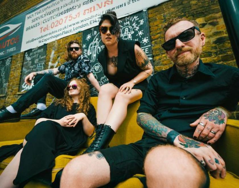 Millie Manders and The Shutup sitting on a sofa outside a mechanic's