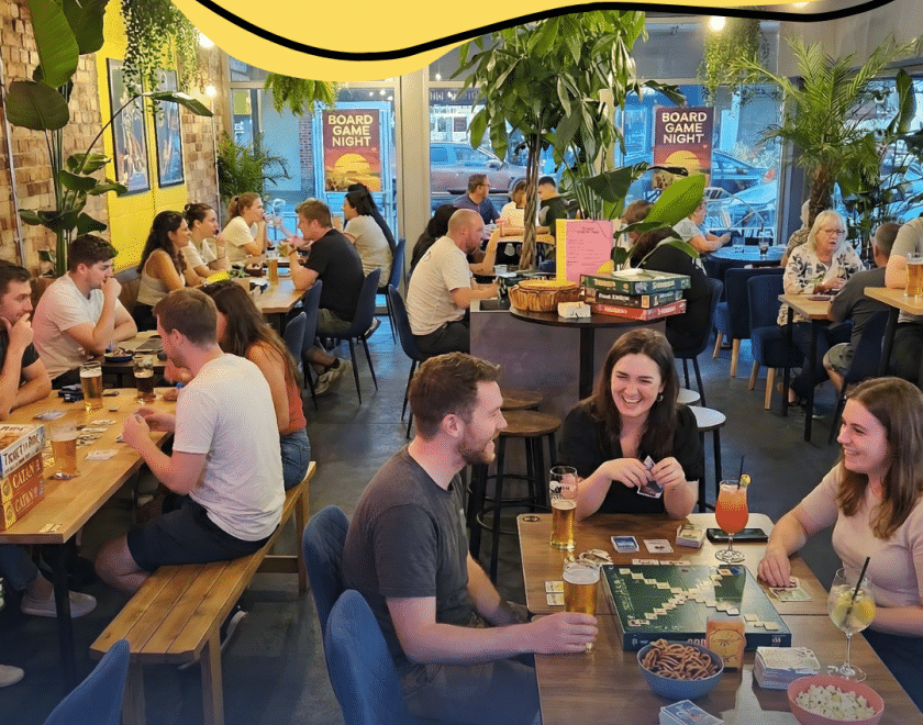 A bustling bar setting with people playing boardgames and having fun - additional information about the event above and below the image