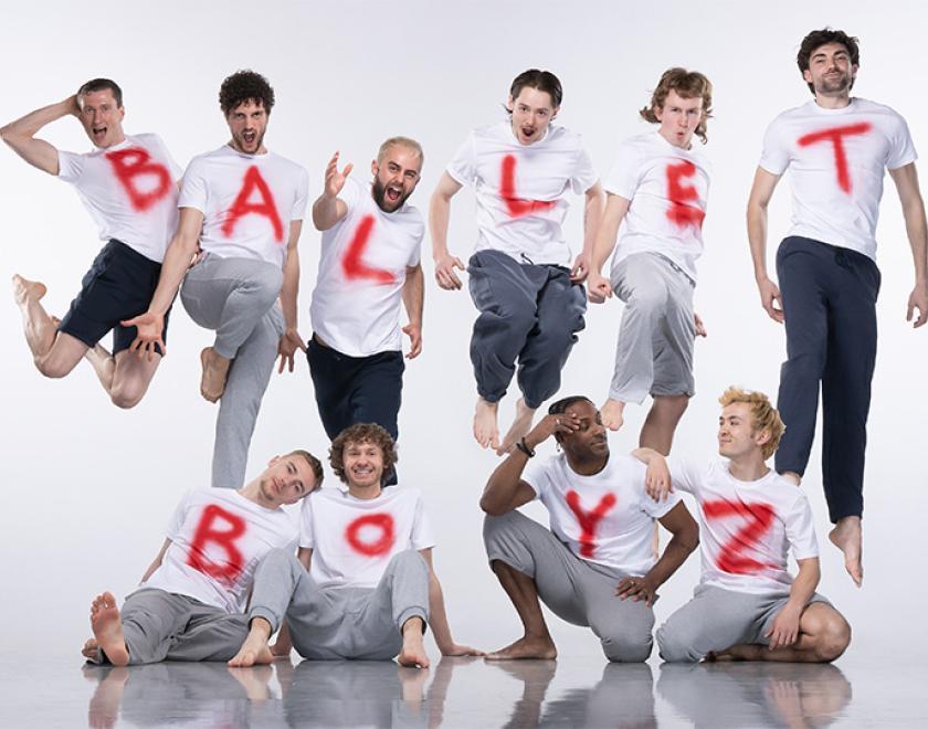 Photo of the Ballet Boyz wearing white t-shirts and dark trousers with red letters spraypainted on them. They're standing in a group so their shirts spell out Ballet Boyz.