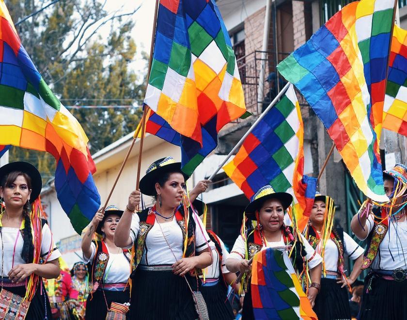 bolivan dancers in black and white outfits, raising colourful flags