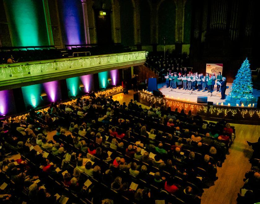 aerial view of Reading Concert Hall showing a capacity crowd seated and a choir on stage, all lit with candles and Christmas lights