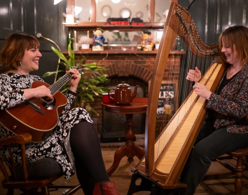 Photo shows two women playing music together on a guitar and a harp