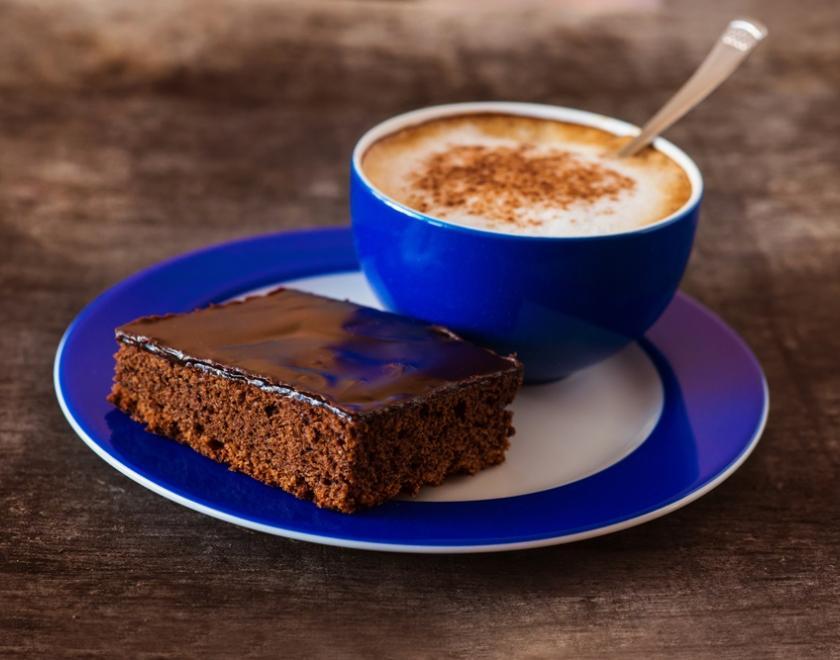 Blue cup and saucer. Coffee in cup and a chocolate brownie on the saucer beside cup.