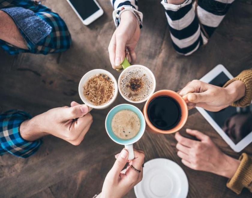 Photograph of four hands holding full coffee cups