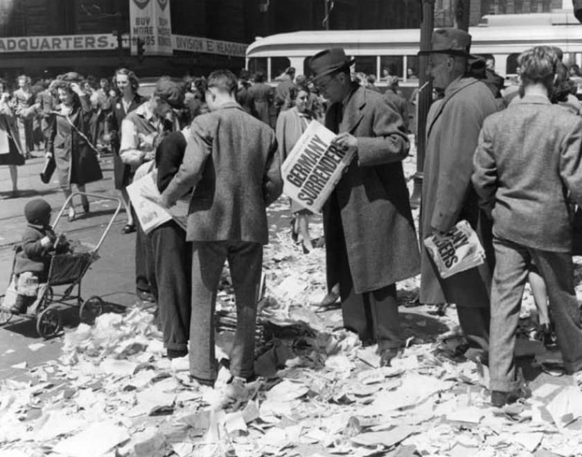 Contemporary image of man reading newspaper with headline Germany Surrenders