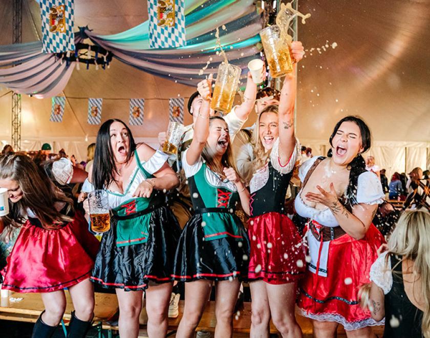 Women in traditional Bavarian fancy dress outfits drinking beer and clinking glasses