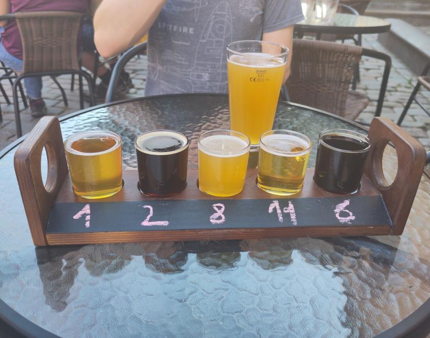 A flight of 5 different beers and a pint in the background