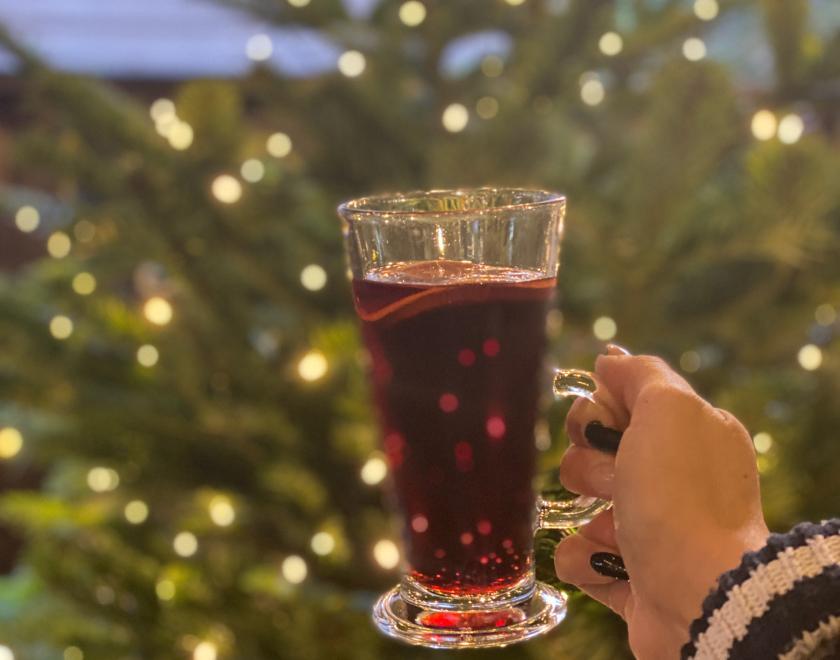 glass of mulled wine with christmas tree and lights behind