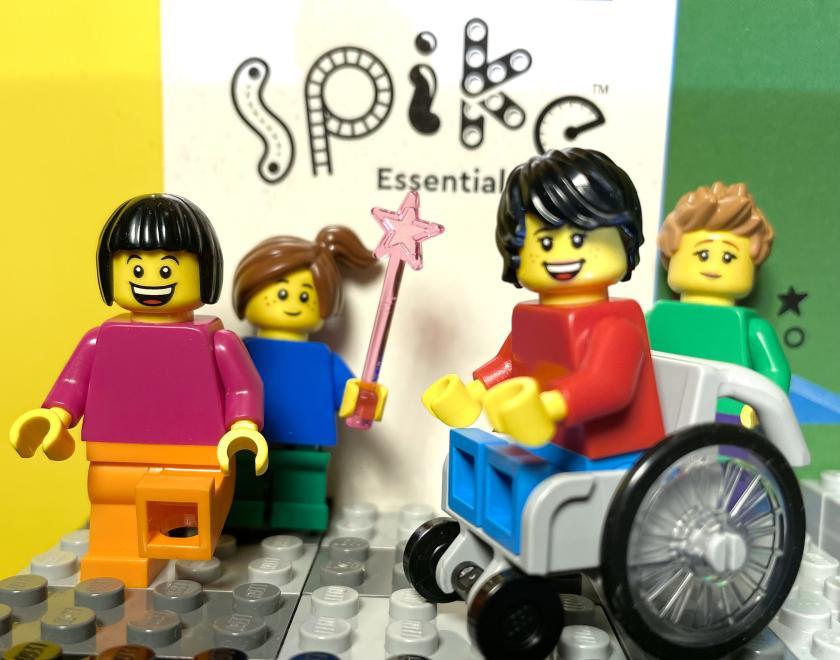Image of poster saying ' LEGO Education Spike Essential' with four LEGO figures ranges in front of , one in a wheelechair