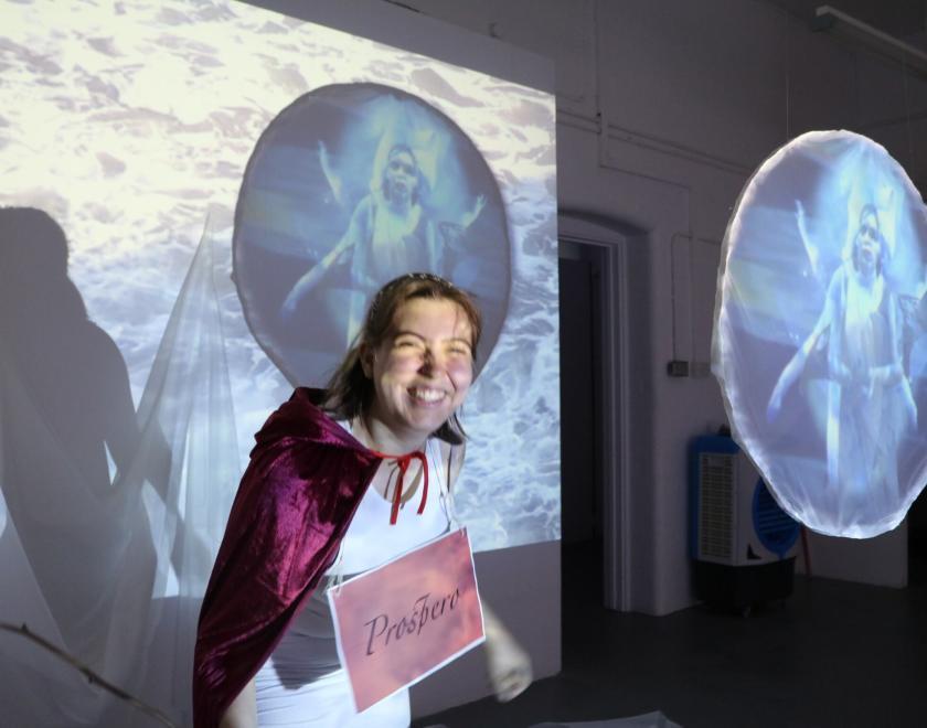 artist wearing red cape in front of projection of their work