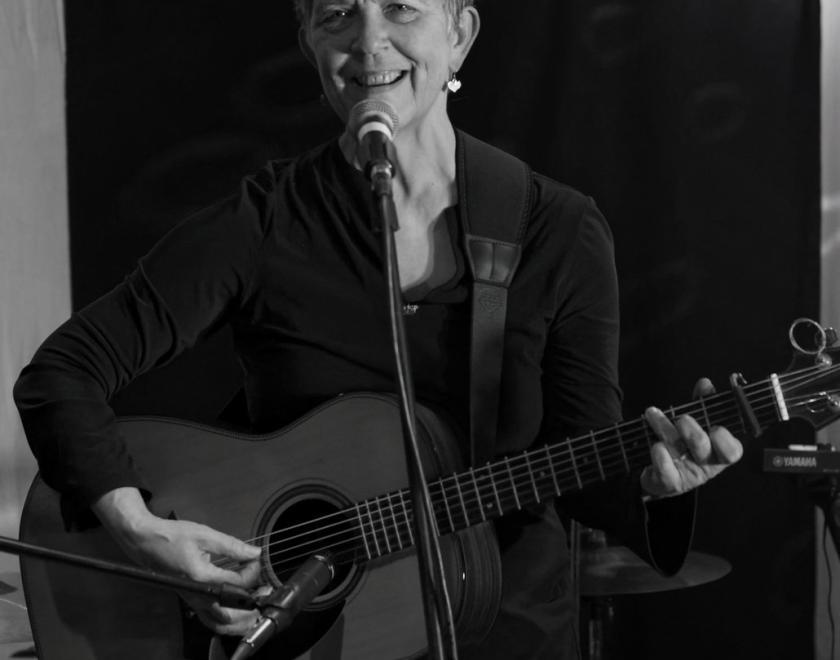 Black and white photograph of Maggie Holland singing and playing guitar