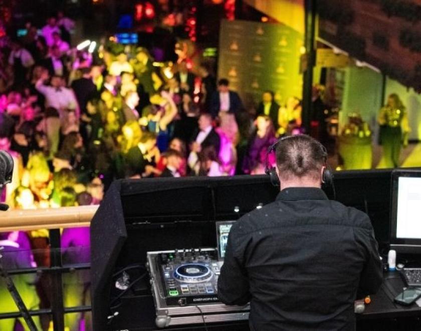 The image shows a DJ playing to a group of people on the dancefloor below.