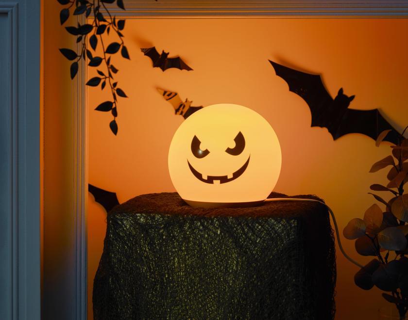 A globe lamp that has been decorated to look like a spooky jack o lantern with bats