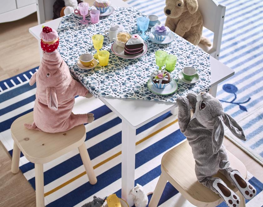 Stuffed animal toys sat around a dressed table having a tea party