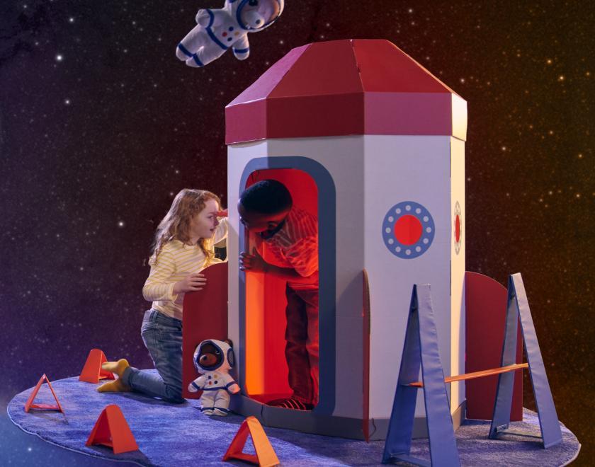 Children playing in a cardboard rocket in space