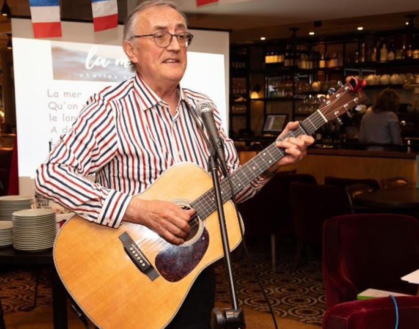 Musician Peter Prowse in a stiped shirt holding an acoustic guitar