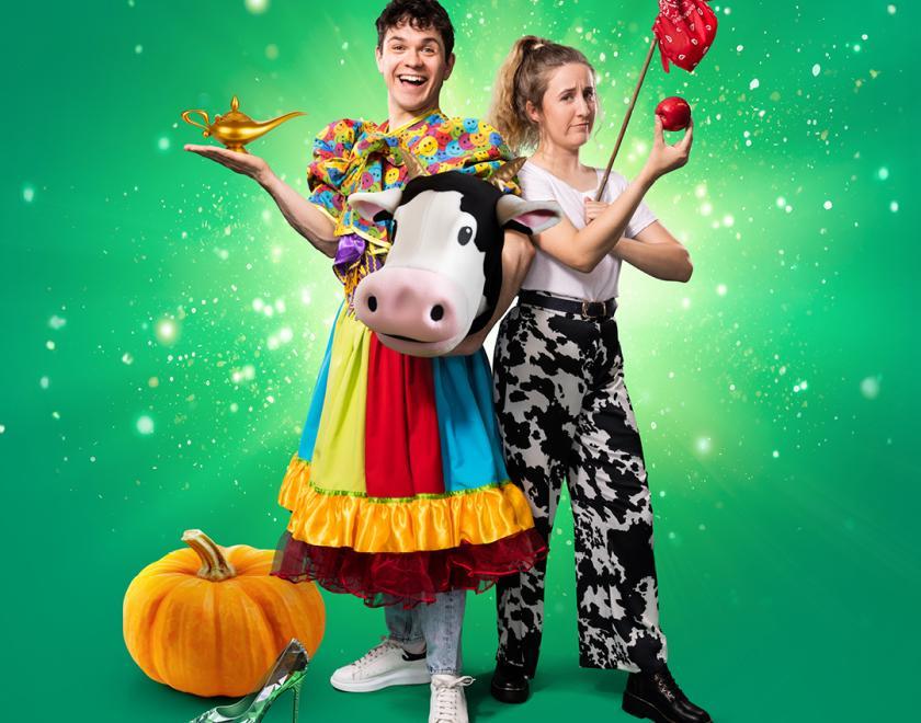 A man in a multi coloured dress, holding a lamp stands next to a woman in a cow costume holding an apple, to their left side is a glass slipper and a pumpkin