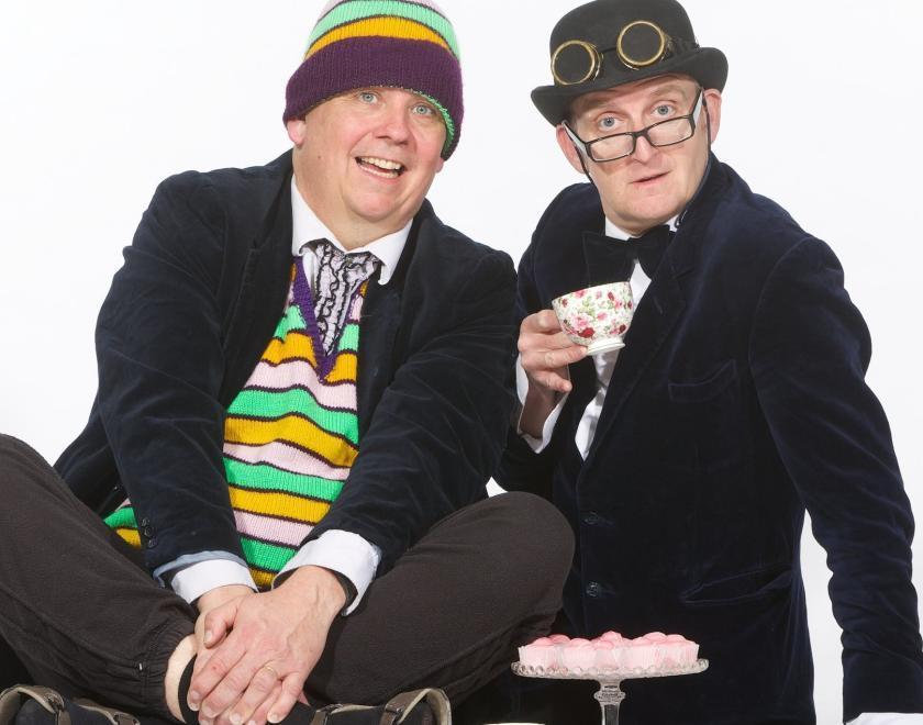 The Raymond and Mr Timpkins Revue dressed in black suits and hats and sitting on the floor - at Just The Tonic Reading