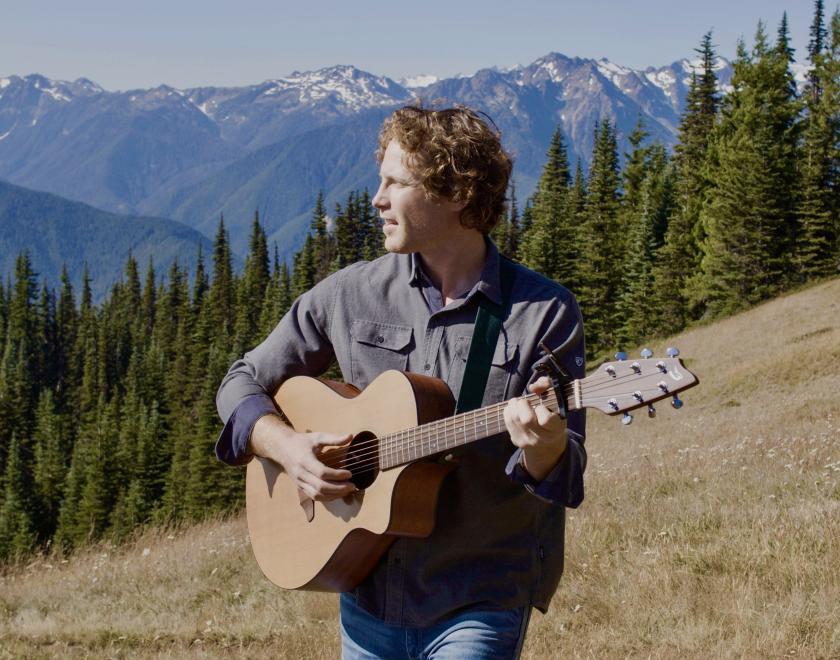 musician Scott Clay stood with a guitar in the mountains