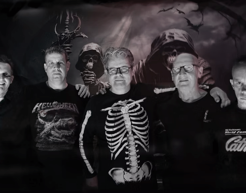 The band Vampire Strikers, five middle-aged men wearing black. The one in the middle has a skeleton printed on his jumper.