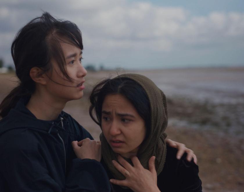 Two young female Hong Kongers huddling together against the windy, grey UK weather