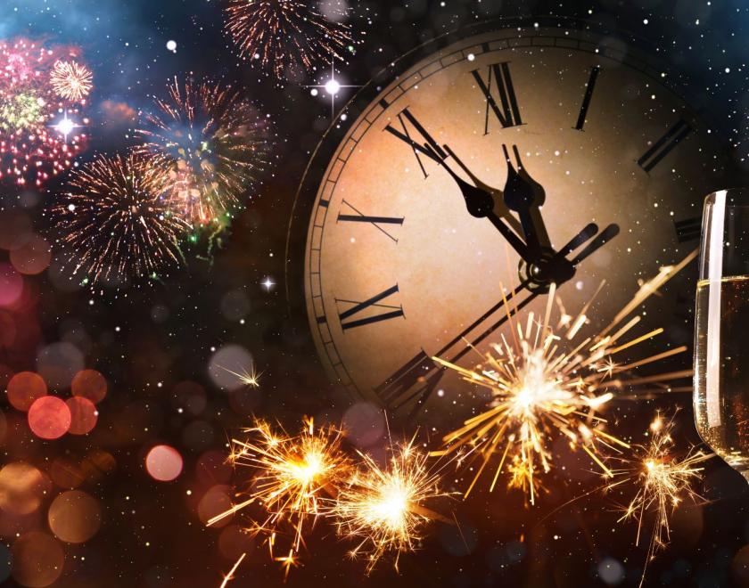 The image is a graphic of a clock face showing five to midnight. There are two glasses of champagne in the corner and fireworks across the whole illustration.