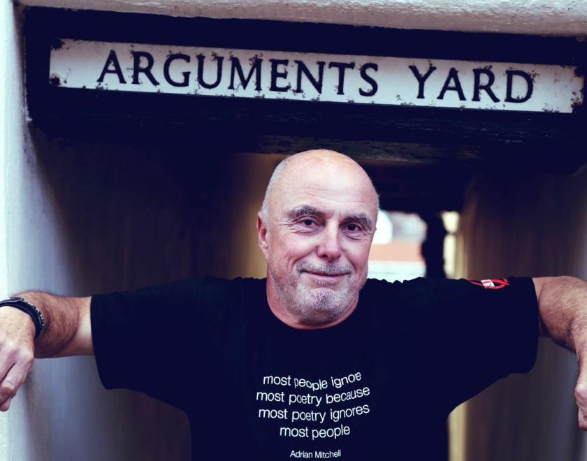 Attila The Stockbroker standing under a street sign saying "Arguments Yard"