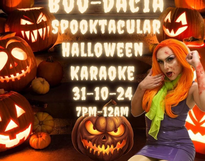 Drag queen dressed as Daphne from scooby Doo in a bright orange wig and purple PVC dress against a background of jack o'lanterns