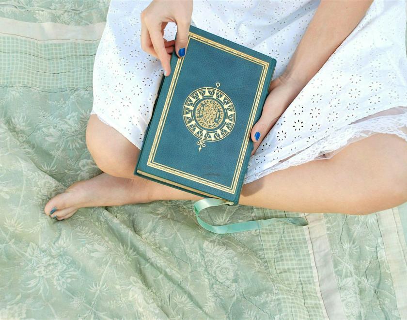 A woman sitting crosslegged with a book on her lap. But we only see her legs and the book.