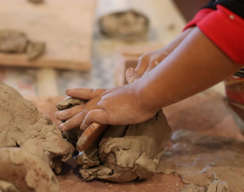 Image of a child's arm and hand kneading clay on a table. 