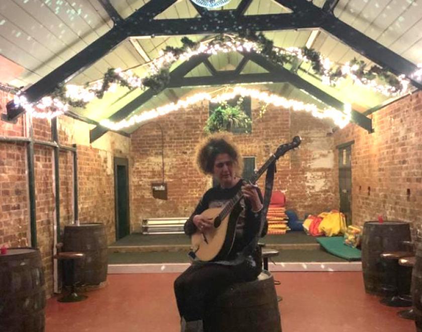 image of singer with a mandola sitting on a beer barrell in a brighlty lit room