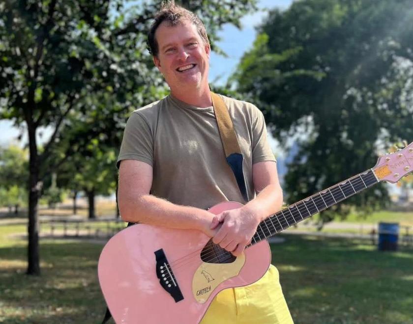 Singer Dick Valentine in a grey t-shirt and yellow shorts, smiling and holding a pink guitar